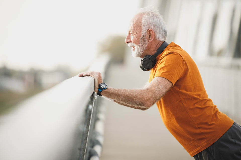Older man in sportswear stretching his leg on a railing