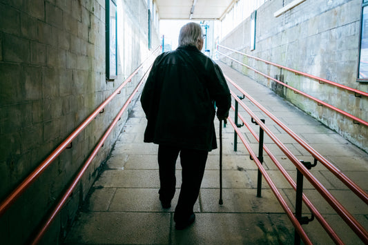 Older person with a walking stick walking along a corridor with handrails