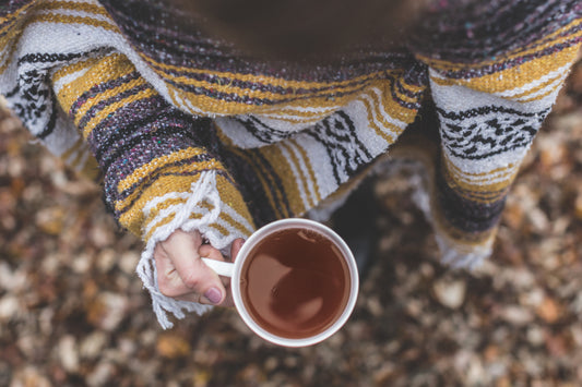 Hand holding a warm cup of tea under a woolen blanket
