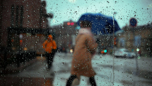 Person with an umbrella walking in the rain, seen through a wet window