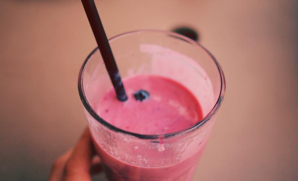Hand holding a glass of pink berry smoothie with a straw