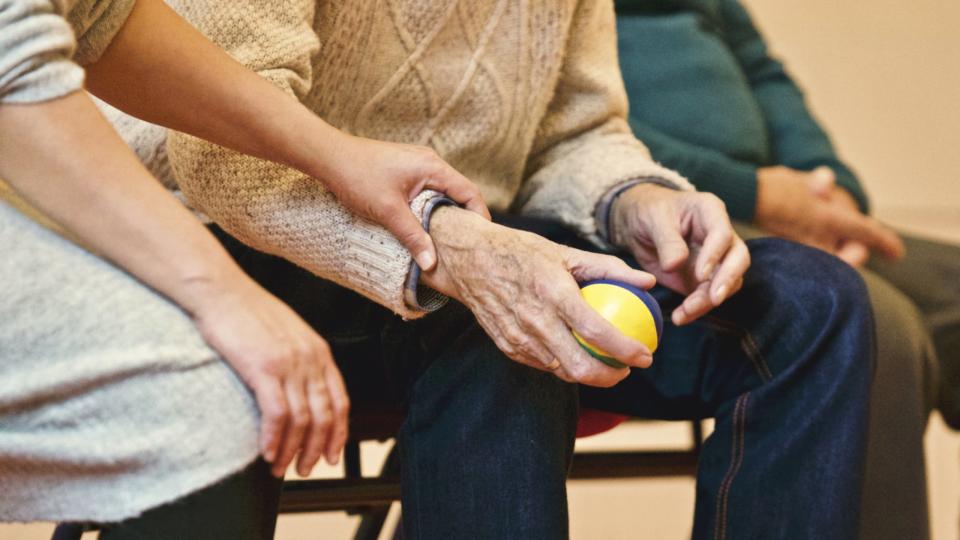 Older person sitting on a chair and holding a small exercise ball